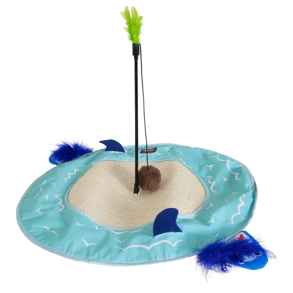 The Mad Cat Desert Island 20 Large Play Mat, a circular interactive cat toy, has a light blue base with printed wave designs, a central scratch mat, and features a feather wand toy with a stick and brown pom-pom. Blue fins and green feathers adorn its edge.