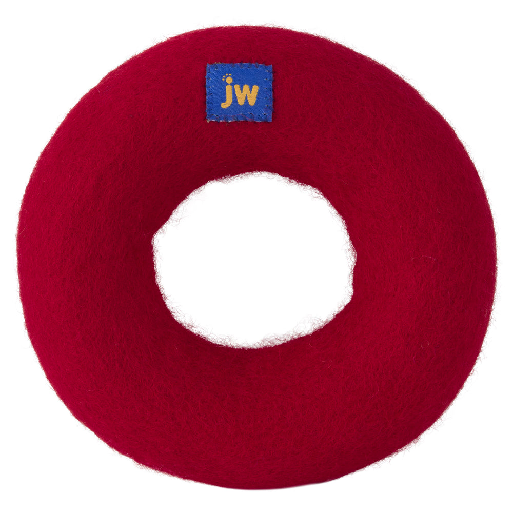 The JW Wool-ee Ring Dog Toy by Jw is a red circular, donut-shaped felt-lined dog toy made from eco-friendly natural wool. It has a small blue square tag with yellow jw letters and a hollow center exposing the white background behind it.