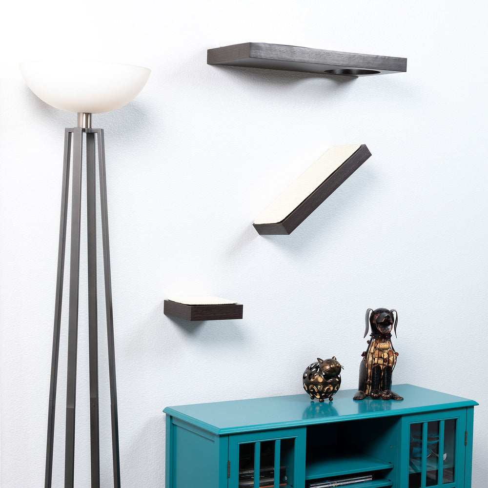 A modern, minimalistic room displays a white floor lamp on the left and three PetFusion Wall Activity Shelves For Cats by Pet Fusion on a pristine wall. Below, a teal cabinet showcases two decorative figurines of a bulldog and an elegant dog.