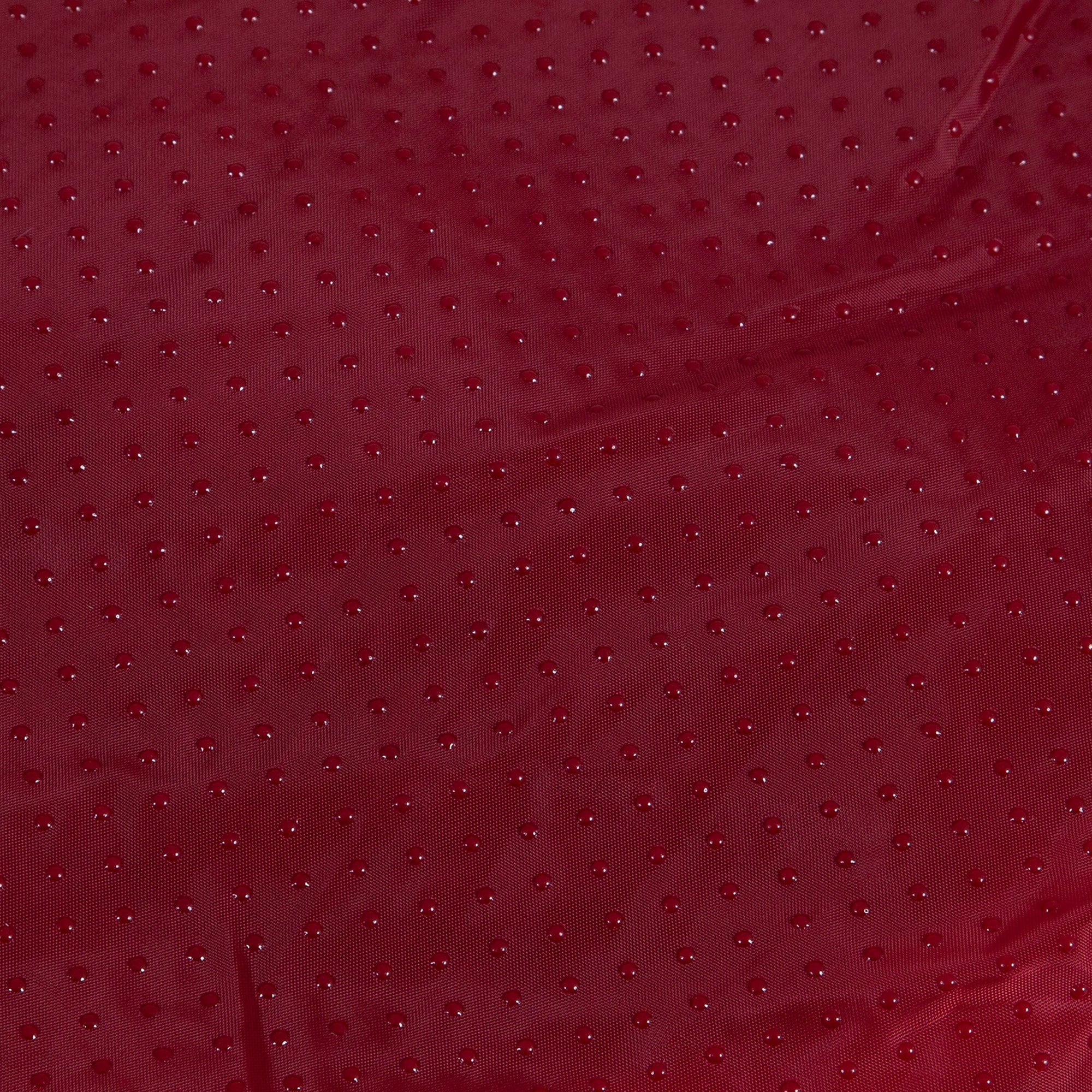 Close-up of the Aspen Pet Self-Warming Oval Lounger Pet Bed featuring a red fabric with a textured dot pattern, resembling faux lambs wool plush. The slightly wrinkled material has a subtle sheen that reflects light, creating a rich, luxurious look.