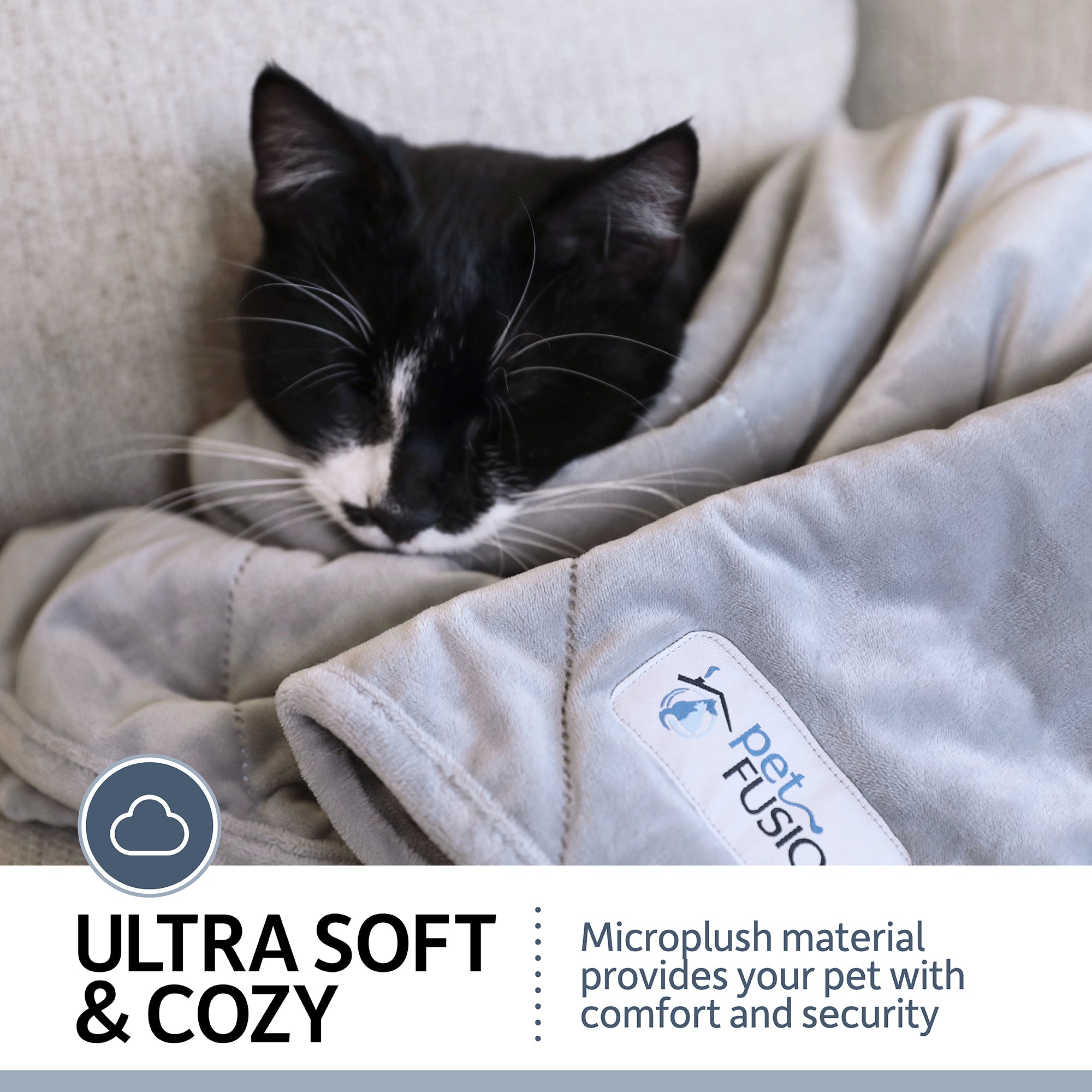 A black and white cat is nestled in a PetFusion Microplush Quilted Dog Blanket on a couch. The blanket, featuring the signature Petfusion logo tag, is ultra-soft and cozy with microplush material for comfort and security, plus its machine-washable for easy maintenance.