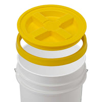 A white HDPE bucket, BPA-free, features a yellow Gamma Seal Lid from Gamma2 with a cross-shaped indentation for an airtight seal. The lid is positioned above the bucket, ready to attach. A sturdy metal handle completes the design.