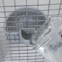 A glass pitcher pours water into the Petmate No Spill Kennel Cup, securely attached to a wire cage interior. The design ensures a smooth flow, efficiently filling the cup for pet hydration.
